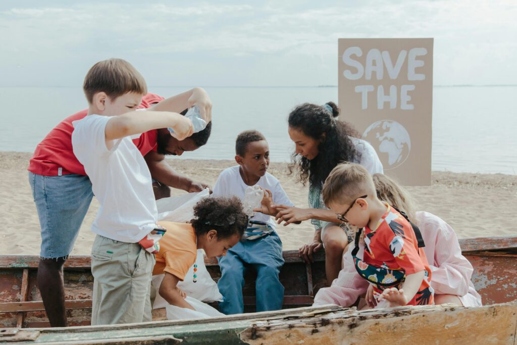 A group of children volunteering to clean a beach with a 'Save the Earth' sign.