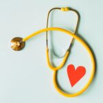 Yellow stethoscope arranged with a red heart cutout on a light green background, symbolizing heart health.